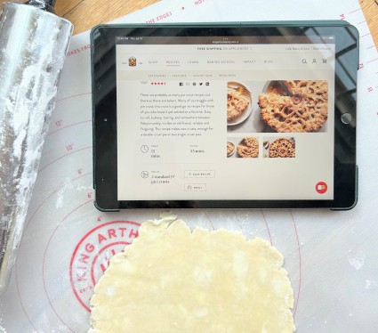 Pie crust rolled on a mat, pictured with a rolling pin and iPad tablet.
