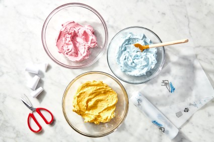 Three bowls of different colored icing: blue, yellow, and pink