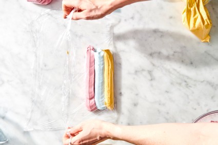 Lines of blue, pink, and yellow frosting piped on plastic wrap