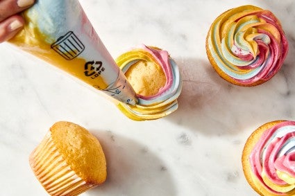 Piping rainbow frosting onto cupcakes