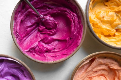 Four bowls of colored frosting in pink, purple, yellow, and orange