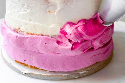 Piping a ring of darker pink frosting on a cake above a ring of lighter pink frosting