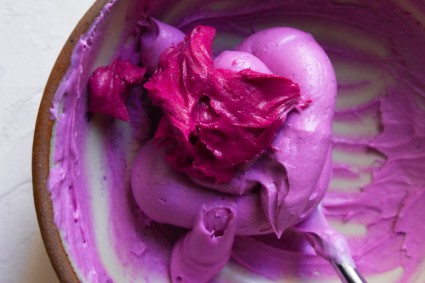 A spoonful of darker pink frosting dolloped on top of lighter pink frosting in a bowl