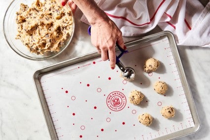 Baker scooping cookie dough onto baking sheet with tablespoon cookie scoop
