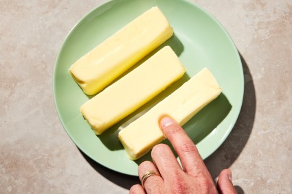 Finger pressing into one of three sticks of softened butter