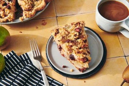 A slice of cherry, almond, and pear pie on a plate next to a cup of coffee.