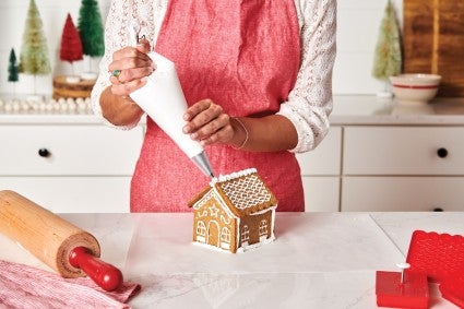Baker assembling roof of gingerbread house with royal icing