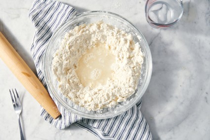 Water poured into well in a bowl of flour and butter, to make pie dough