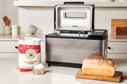 Loaf of bread and bag of flour in front of bread machine