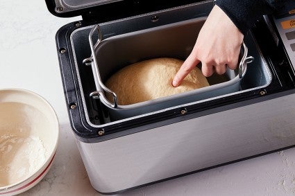 Baker pressing finger into loaf of proofing bread in a bread machine