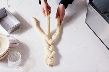 Baker braiding bread dough next to bread machine