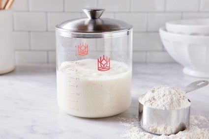 Glass sourdough crock next to measuring cup full of flour