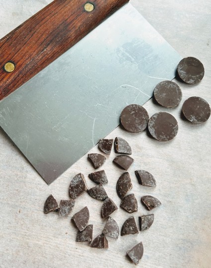 A bench knife showing how it chops round disks of solid chocolate into four even quarters each.