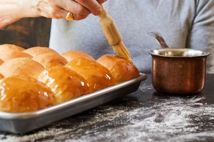 A baker brushing freshly baked dinner rolls with butter