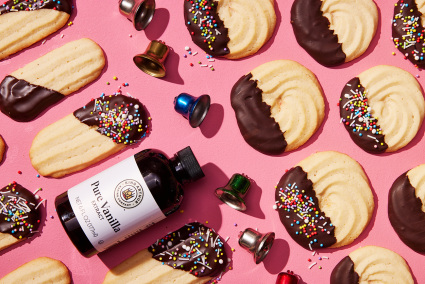 Cookies lined up on a pink background with a bottle of vanilla extract. 