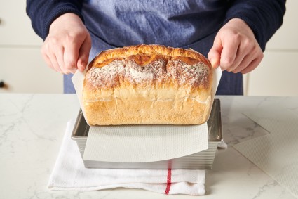 Baker lifting loaf of bread out of pan using loaf pan liner