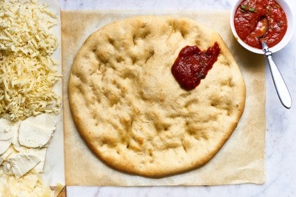 Par-baked pizza crust being topped with tomato sauce