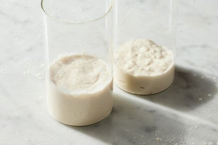 Ripe sourdough starter in a glass container next to just-fed starter in a glass container