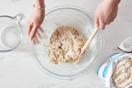 Baker stirring a bowl of bread dough that has formed a shaggy mass