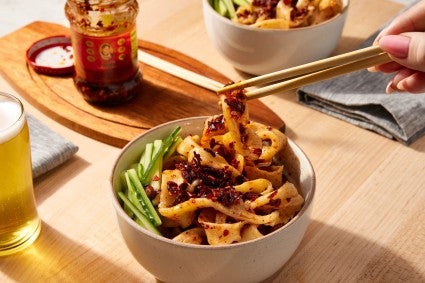 Bowl of biang biang noodles garnished with chili crisp and cucumber being eaten with chopstocks