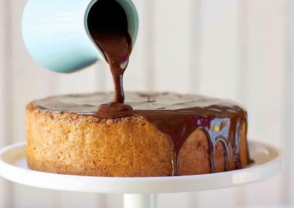 Chocolate ganache being poured over a single round layer of yellow cake. 