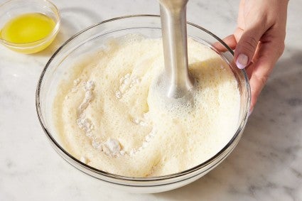 A baker using an immersion blender to make smooth popover batter