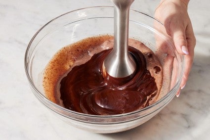 A baker using an immersion blender to make smooth chocolate ganache