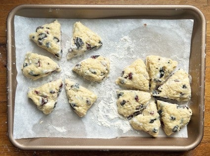 Two discs of scone dough on a parchment-lined baking sheet, each cut into six wedges, the wedges pulled slightly apart, ready to go into the oven.