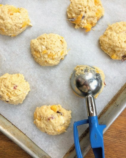 Soft scone batter being dropoped onto a parchment-lined baking sheet to make drop scones.