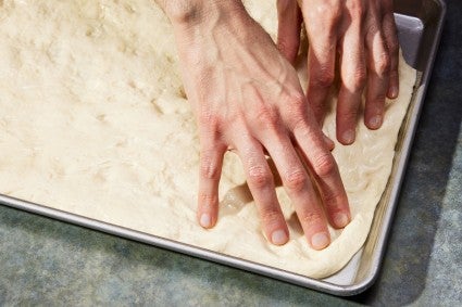 Baker pressing pizza dough into a rectangular pan