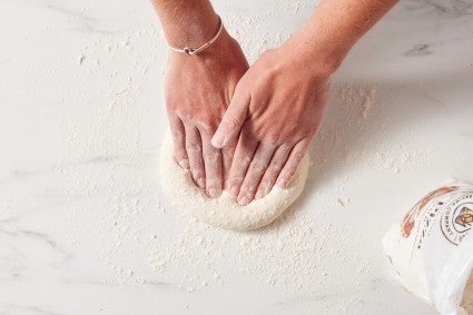 Baker using hands to push a small circle of pizza dough outwards
