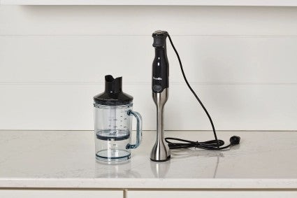 A Breville Control Grip Immersion Blender on a counter top next to the blending jug that comes with it