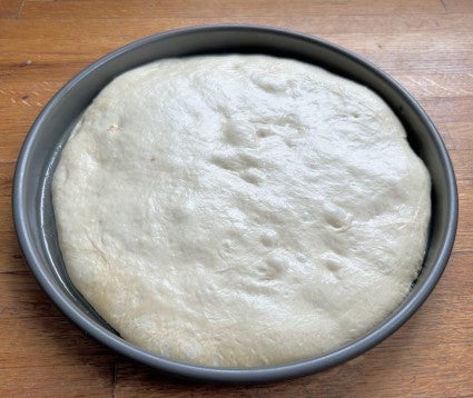 Risen pizza dough in a round pan, ready to top and bake.