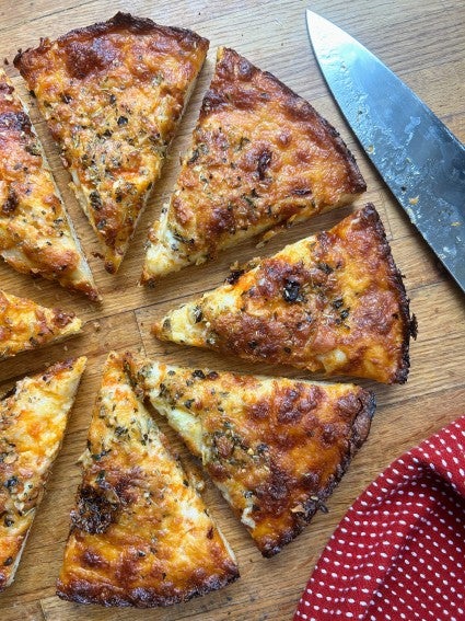 Hot from the oven round piza on a wooden cutting board, sliced into eight wedges.