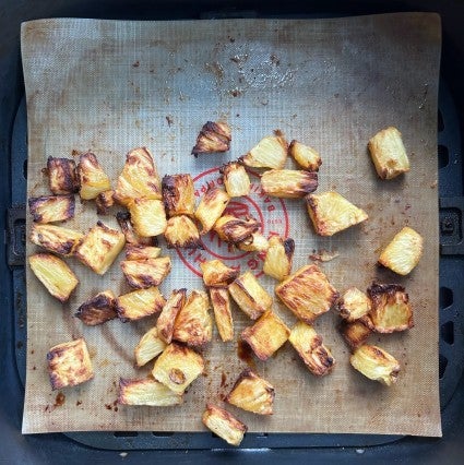 Diced browned pineapple in the basket of an air fryer.