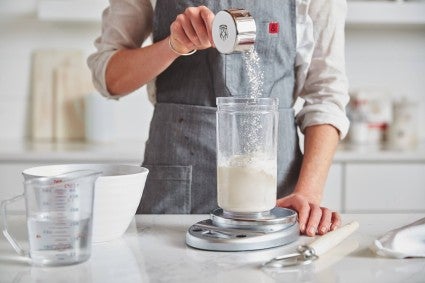 Flour being measured into a jar of sourdough starter, as part of the feeding process. 