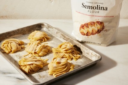 Nests of semolina flour on a baking sheet, in front of a bag of semolina flour