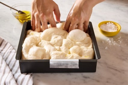 Dimpling focaccia dough in a focaccia pan