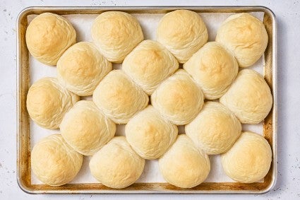 Top down photograph of dinner rolls partially baked on a sheet tray.