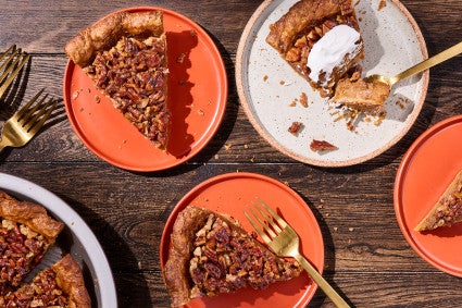Pumpkin pecan pie slices shown on plates scattered around a rustic wooden table.