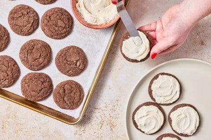 Overhead photograph of hands applying frosting to soft chocolate sugar cookies.