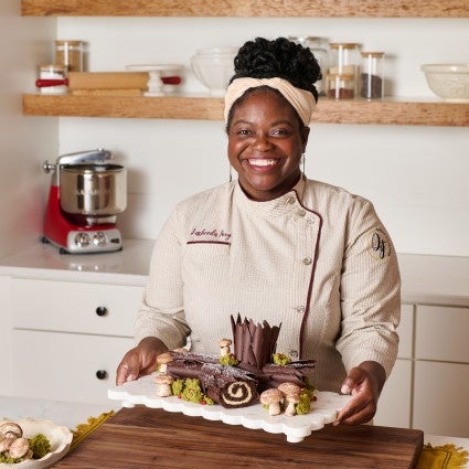 Pastry chef Lasheeda Perry in a kitchen holding a chocolate buche de noel