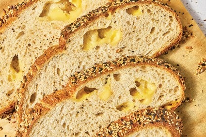 Detail of Parmesan Black Pepper Sourdough Bread sliced and laid out on a wooden cutting board showing an airy bread with cheese in the air pockets.