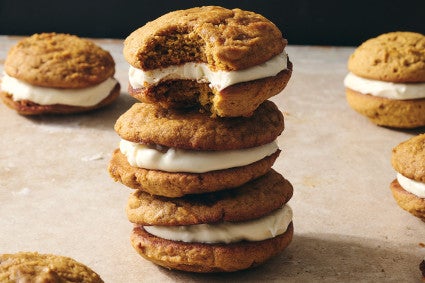 Pumpkin Whoopie Pies photographed in a stack on a counter showing the layers of pumpkin cookie and creamy filling.