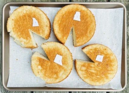 Four round layers of chiffon cake on a parchment-lined baking sheet, each with a slice removed to check for height. 