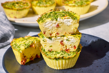 Egg Bites stacked on a plate with a cross-section showing a quiche like interior with greens, cottage cheese, and red pepper.