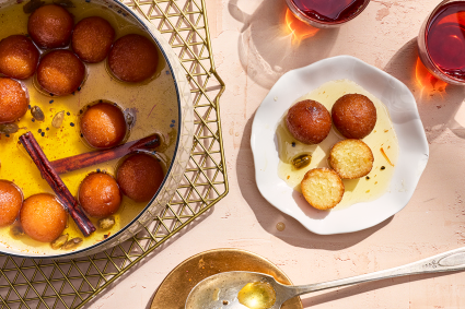 Gulab Jamun in a bowl with the fragrant syrup and some on a plate.