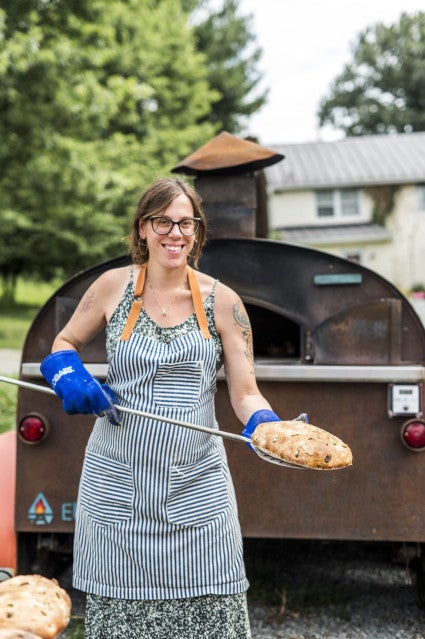 Baker Tara Jensen baking pizza and holding a peel in front of a wood-fired oven