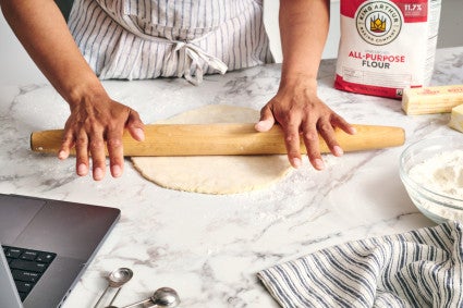 Baker rolling out pie dough next to a bag of all-purpose flour 