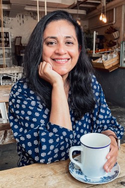 Shilpa seated at a table with a mug